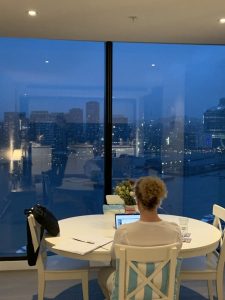 woman sitting at laptop at large window with city view Generative Change Life Changing Coaching Online and By Phone